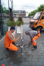 Sascha Kube und Klaus Maienschein (rechts) vom städtischen Eigenbetrieb Hanau Infrastruktur Service (HIS) montieren auf der Südwestseite des Marktplatzes einen von zehn neuen Radbügeln